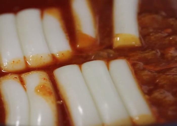 Sau đó, cho thêm hành tây và chả cá cắt nhỏ vào chảo.